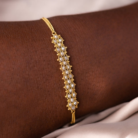 This delicate 18k yellow gold chain bracelet features three rows of woven silver diamonds in the center. The bracelet is finished with a lobster clasp closure.