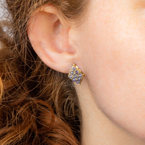 A model wears an earring crafted in 18k yellow gold chain and tanzanite stones that are woven into a diamond lattice pattern and fastened with a post closure.