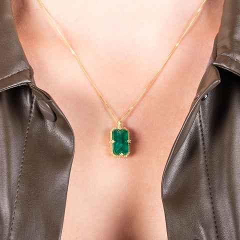 A medium faceted rectangular emerald is set in an 18k yellow gold chain wrapped bezel with four beaded prongs on a short delicate chain.