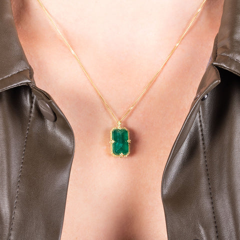 A medium faceted rectangular emerald is set in an 18k yellow gold chain wrapped bezel with four beaded prongs on a short delicate chain.