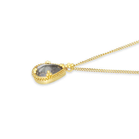 A side view of a small teardrop shaped grey diamond pendant is set in an 18k yellow gold chain wrapped bezel with four beaded prongs. The pendant hangs on a delicate short chain.