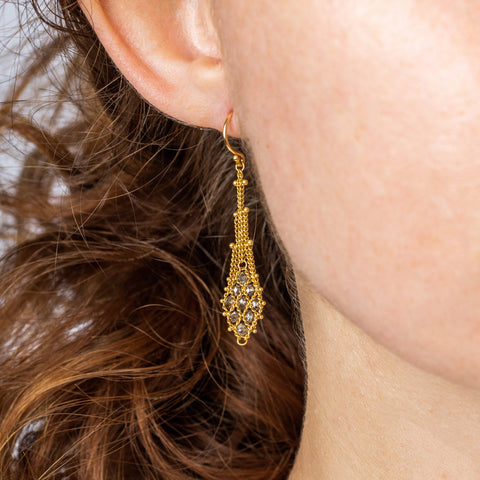 A model wears an earring crafted in 18k yellow gold chain and champagne diamonds that are woven into a diamond lattice pattern.