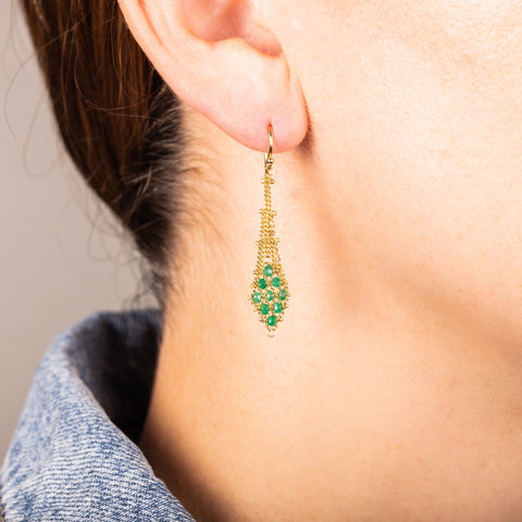 A model wears an earring crafted in 18k yellow gold chain and emerald beads that are woven into a diamond lattice pattern.