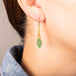 A model wears an earring crafted in 18k yellow gold chain and emerald beads that are woven into a diamond lattice pattern.