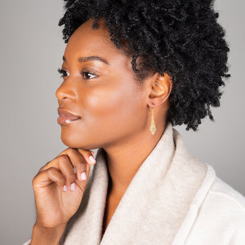 A model wears an earring crafted in 18k yellow gold chain and silver diamonds that are woven into a diamond lattice pattern.
