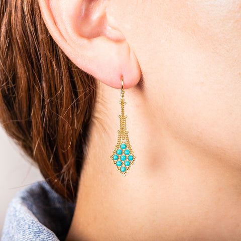 A model wears an earring crafted in 18k yellow gold chain and turquoise stones that are woven into a diamond lattice pattern.