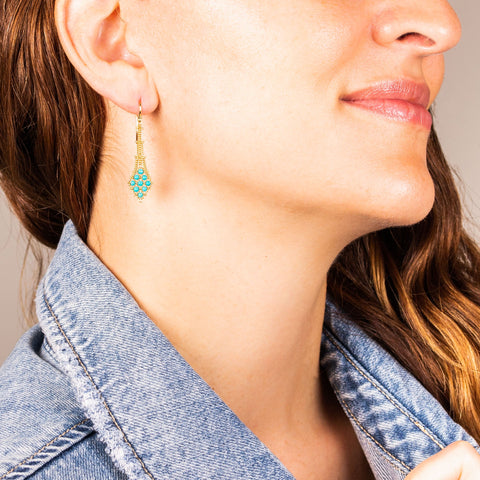 A model wears an earring crafted in 18k yellow gold chain and turquoise stones that are woven into a diamond lattice pattern.