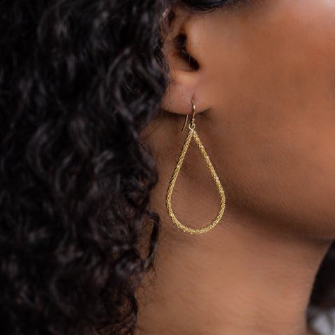 A model wears a large teardrop shaped 18k yellow gold earring with a stardust-like finish.