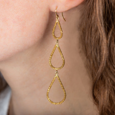 A model wears a long 18k yellow gold earring with three teardrops crafted in chain to create a stardust-like effect.