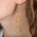 A model wears a long 18k yellow gold earring with three teardrops crafted in chain to create a stardust-like effect.