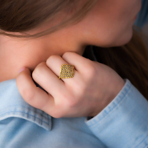 A model wears an 18k yellow gold ring crafted with grey diamond beads that are woven into a diamond shaped lattice pattern.