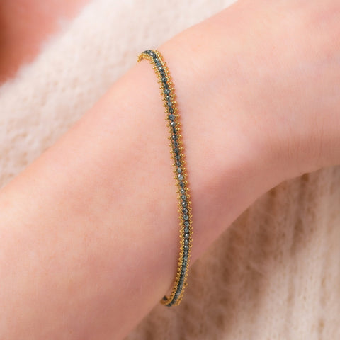 This delicate 18k yellow gold bracelet is delicately woven with blue diamond beads throughout. The bracelet is finished with an 18k yellow gold lobster clasp.