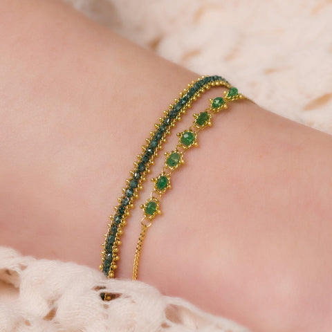 A model wears two 18k yellow gold bracelets, one featuring blue diamonds and one with emeralds.