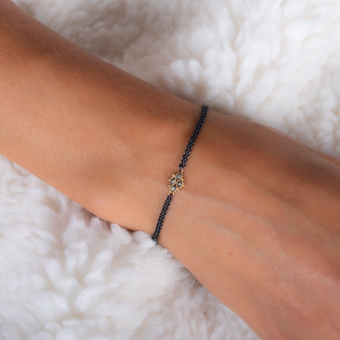 A model wears an oxidized sterling silver bracelet with an 18k yellow gold and grey diamond lattice in the center.