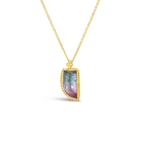 A small dagger shaped watermelon tourmaline pendant, with dark blue and pink hues, is set in an 18k yellow gold chain wrapped bezel. The stone hangs on a delicate chain.