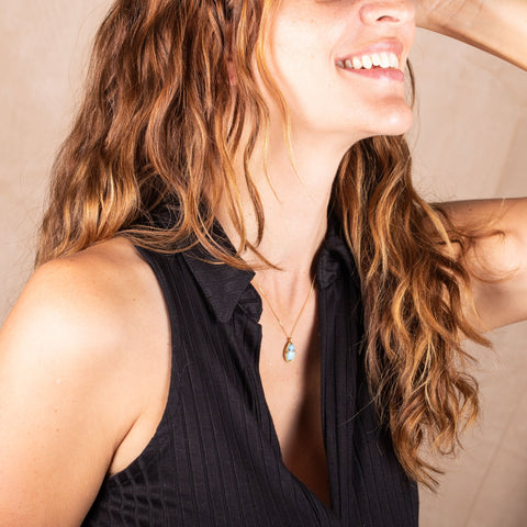 A model wears a small turquoise pendant that is set in 18k yellow gold on a short chain.