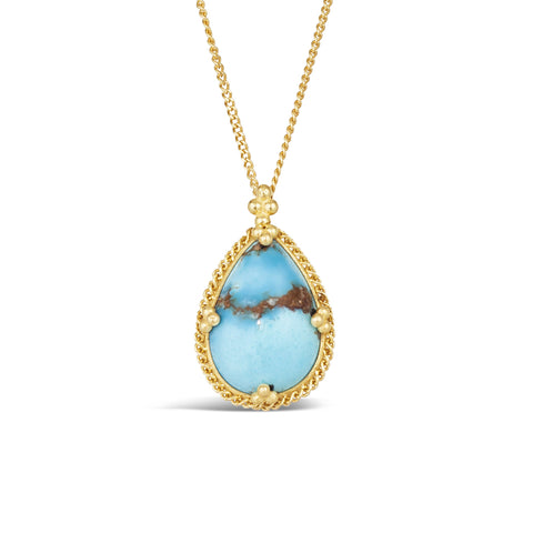 A teardrop shaped turquoise necklace features a dark brown vein across the center of the stone. The stone is set in 18k yellow gold with a braided bezel and granulated prongs on a short chain.