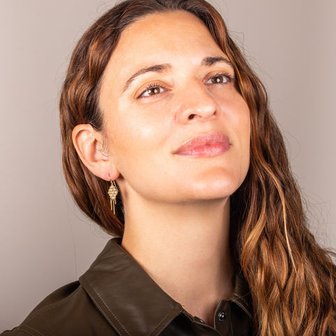 A model wears an 18k yellow gold earring crafted with silver diamonds woven into a diamond shaped lattice pattern and has three dangling chains at the bottom.