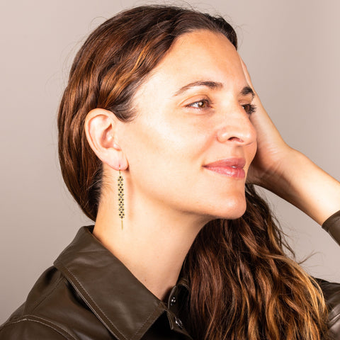 A pair of long black diamond earrings features a woven lattice pattern and two dangling chains at the bottom of the earring. The earrings fasten with french hook closures.