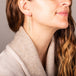 A model wears a long white pearl earring featuring a woven lattice pattern and two dangling chains at the bottom. The earring. fasten with french hook closure.