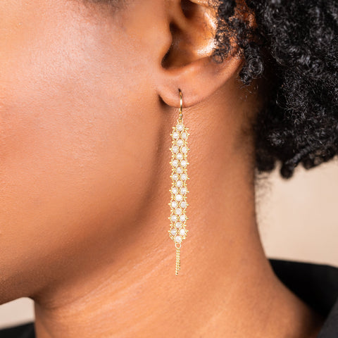 A pair of long grey diamond earrings features a woven lattice pattern and two dangling chains at the bottom of the earring. The earrings fasten with french hook closures.