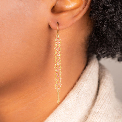 A pair of long red spinel earrings features a woven lattice pattern and two dangling chains at the bottom of the earring. The earrings fasten with french hook closures.