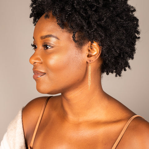 A model wears a long red spinel earring featuring a woven lattice pattern and two dangling chains at the bottom. The earring. fasten with french hook closure.