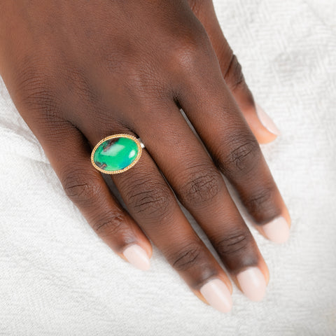 A gold and silver ring featuring an oval gem silica stone on a person's finger
