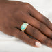 An oval ring featuring a light blue-green opal stone in a gold setting, with a silver-toned band, shown on a person's finger.