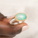 An oval ring featuring a light blue-green opal stone in a gold setting, with a silver-toned band held in hand