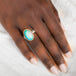 Hand wearing a ring with an Ethiopian opal gemstone set in a gold bezel with a silver band on a white background