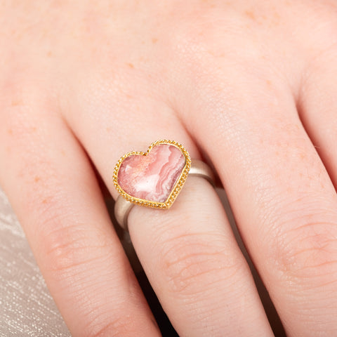 Heart-shaped ring with rhodochrosite stone, gold setting and silver band on a person's finger