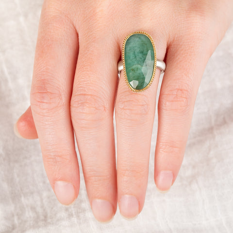 A hand wearing an emerald ring with a gold bezel and sterling silver band