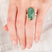A hand wearing an emerald ring with a gold bezel and sterling silver band