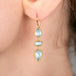 Gold earrings with blue aquamarine gemstones worn by a person