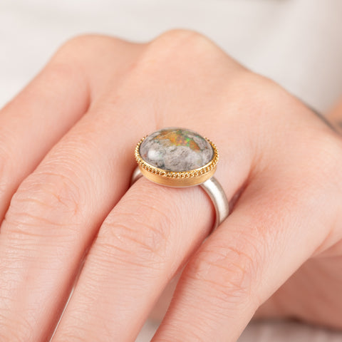 Close up of a handmade ring on a finger with a mexican opal stone, gold setting and sterling silver band