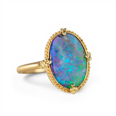 Gold ring with a colorful boulder opal stone on a white background