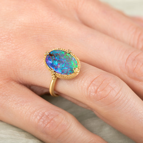 Gold ring with a colorful boulder opal stone on a hand