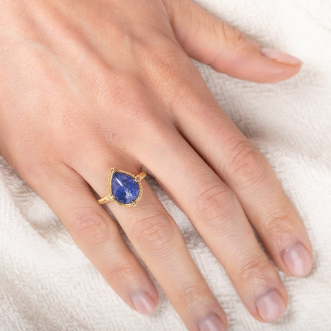 Gold ring with a teardrop-shaped tanzanite gemstone on a person's finger