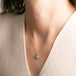 A gold chain necklace with a square pendant featuring an apatite stone set in an 18k bezel, worn on a person's neck.