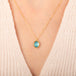 A gold chain necklace with an oval pendant featuring an apatite stone set in an 18k bezel, worn on a person's neck.