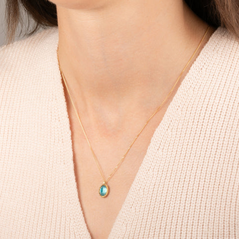 A gold chain necklace with an oval pendant featuring an apatite stone set in an 18k bezel, worn on a person's neck.
