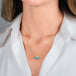 A gold chain necklace with a rectangular, aquamarine gemstone pendant, shown worn on a model's neck.