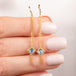 A pair of gold dangle earrings with textured chains leading to aquamarine gemstones, shown held in hand.