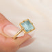 A square-cut light blue aquamarine ring set in an 18k gold bezel, held in hand.