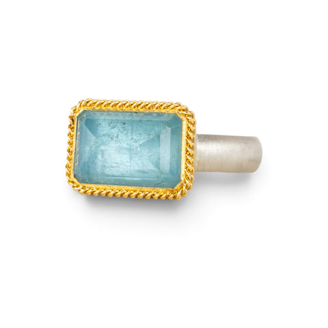 Handmade ring featuring an aquamarine gemstone set in an 18k gold bezel and paired with a sterling silver band, against a white background.