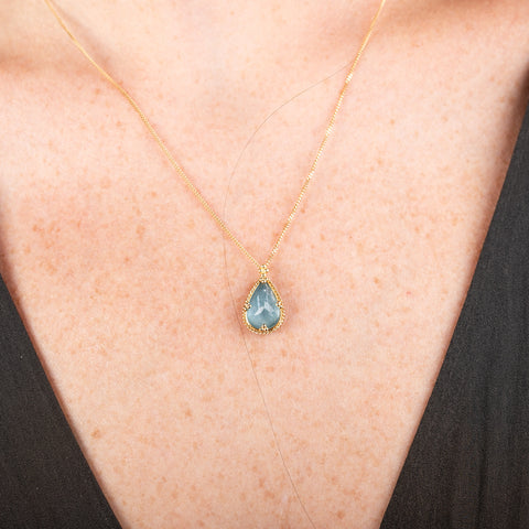 Gold necklace with a teardrop-shaped aquamarine pendant on a person