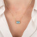 Gold necklace with an aquamarine gemstone pendant worn by a person in a white shirt.