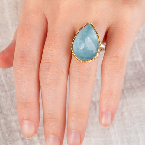 Hand wearing an aquamarine ring with gold bezel and sterling silver band on white background