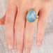 Hand wearing an aquamarine ring with gold bezel and sterling silver band on white background